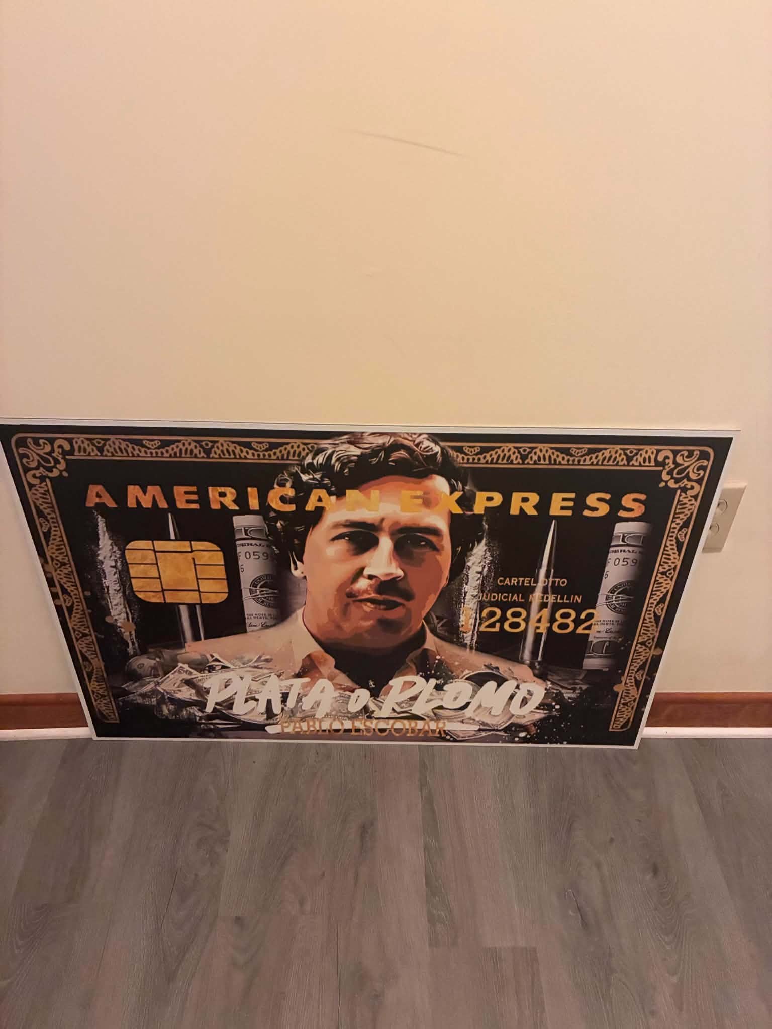 Photo of an American Express black card art print styled with stacked cash and gold money motifs under the phrase Plata o Plomo